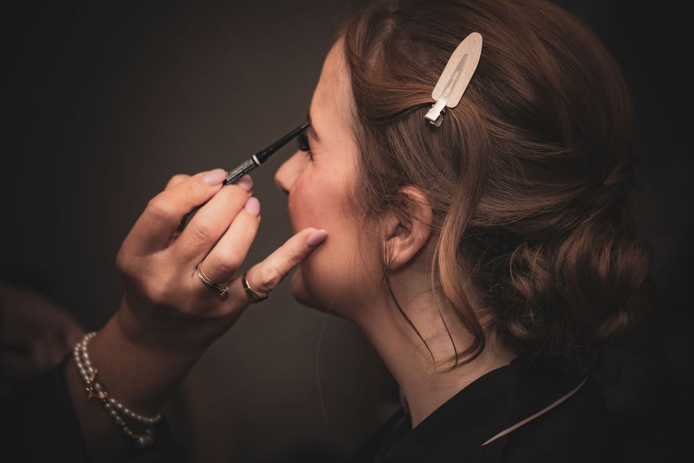 Makeup artist applies cosmetics with brush in dramatic side profile lighting against dark background.