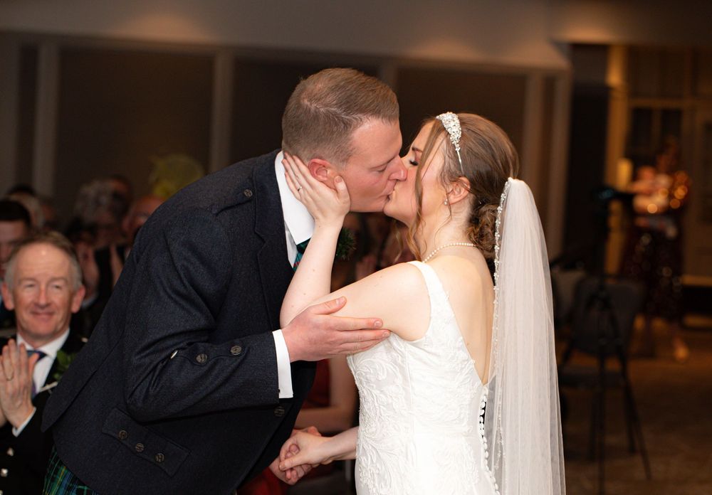 A romantic wedding kiss moment captured in warm lighting during an evening reception celebration.