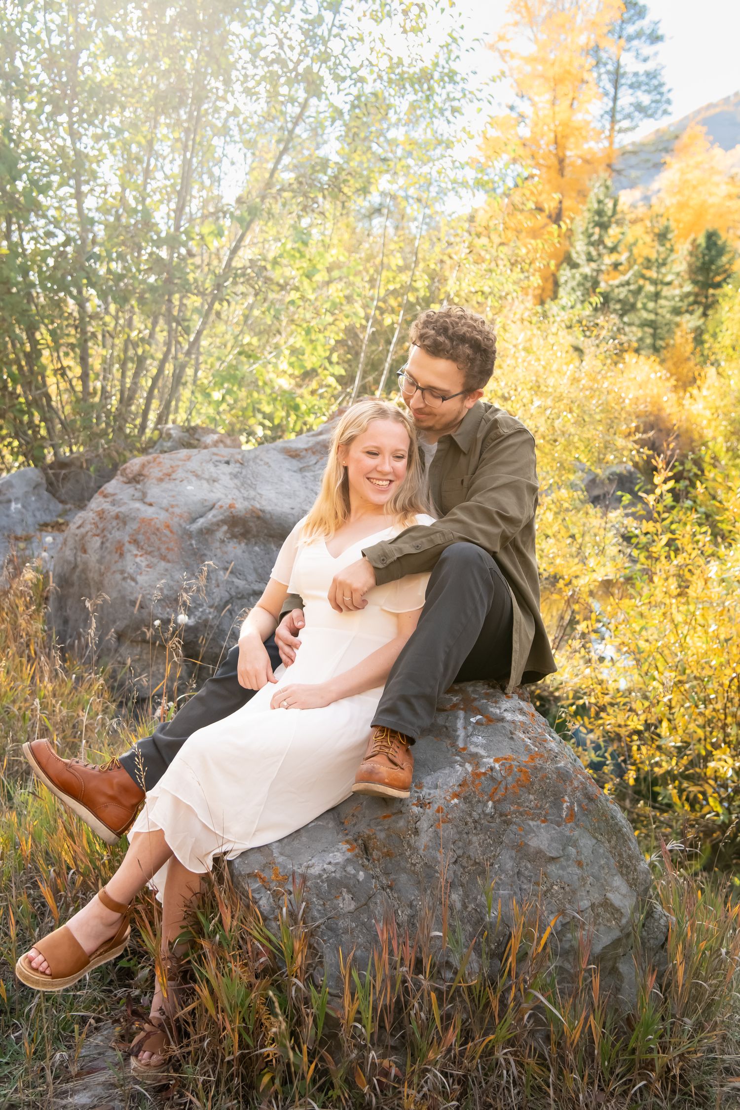 Cute couple sitting intimately on a rock with fall foliage behind them during fall engagement session in Vail Colorado