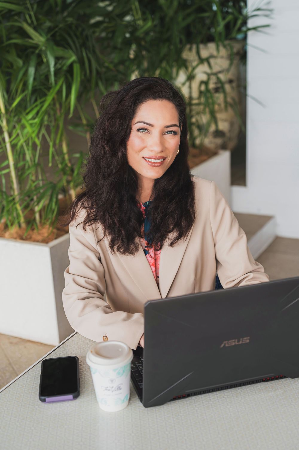 Professional working on an Asus laptop at a modern workspace with coffee and greenery in the background.