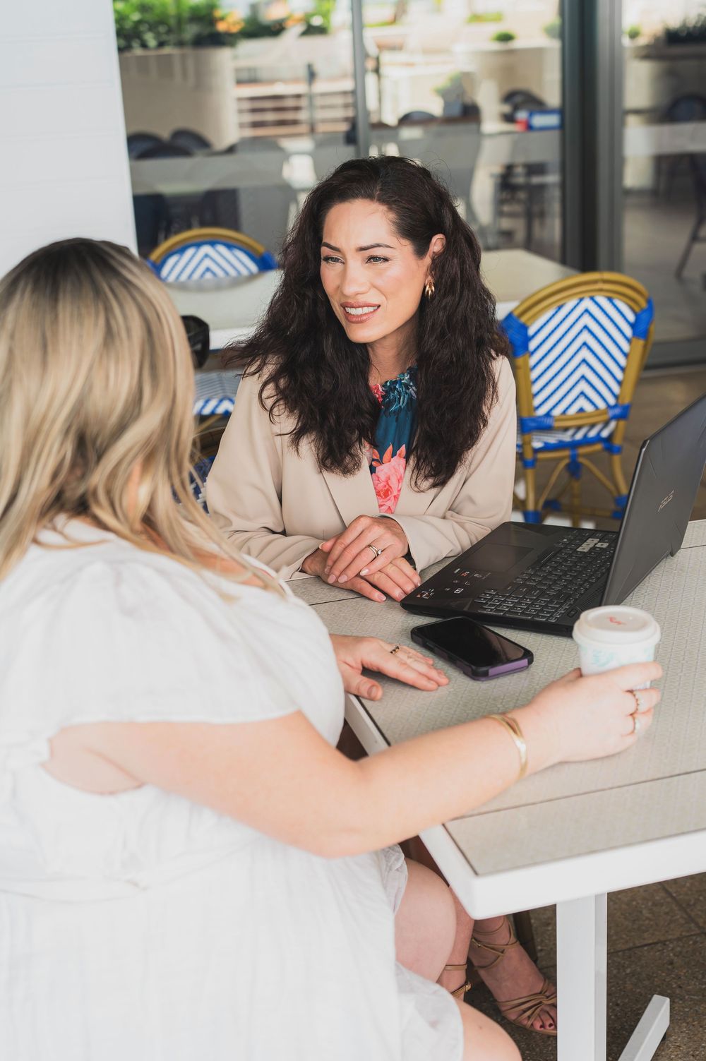 Two people collaborating at a white desk with laptops and coffee cups during a business meeting.