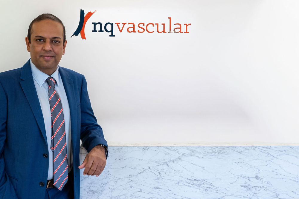 Professional in a navy suit and striped tie poses against a white background in a corporate setting.