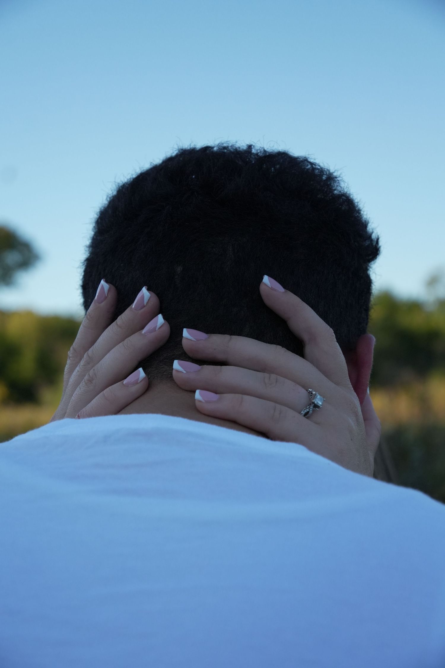 Close-up of a womans hands with French manicure and engagement ring resting on a mans head.