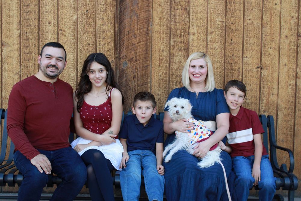 Family wearing coordinated red and navy blue outfits poses together on wooden fence for outdoor portrait session.