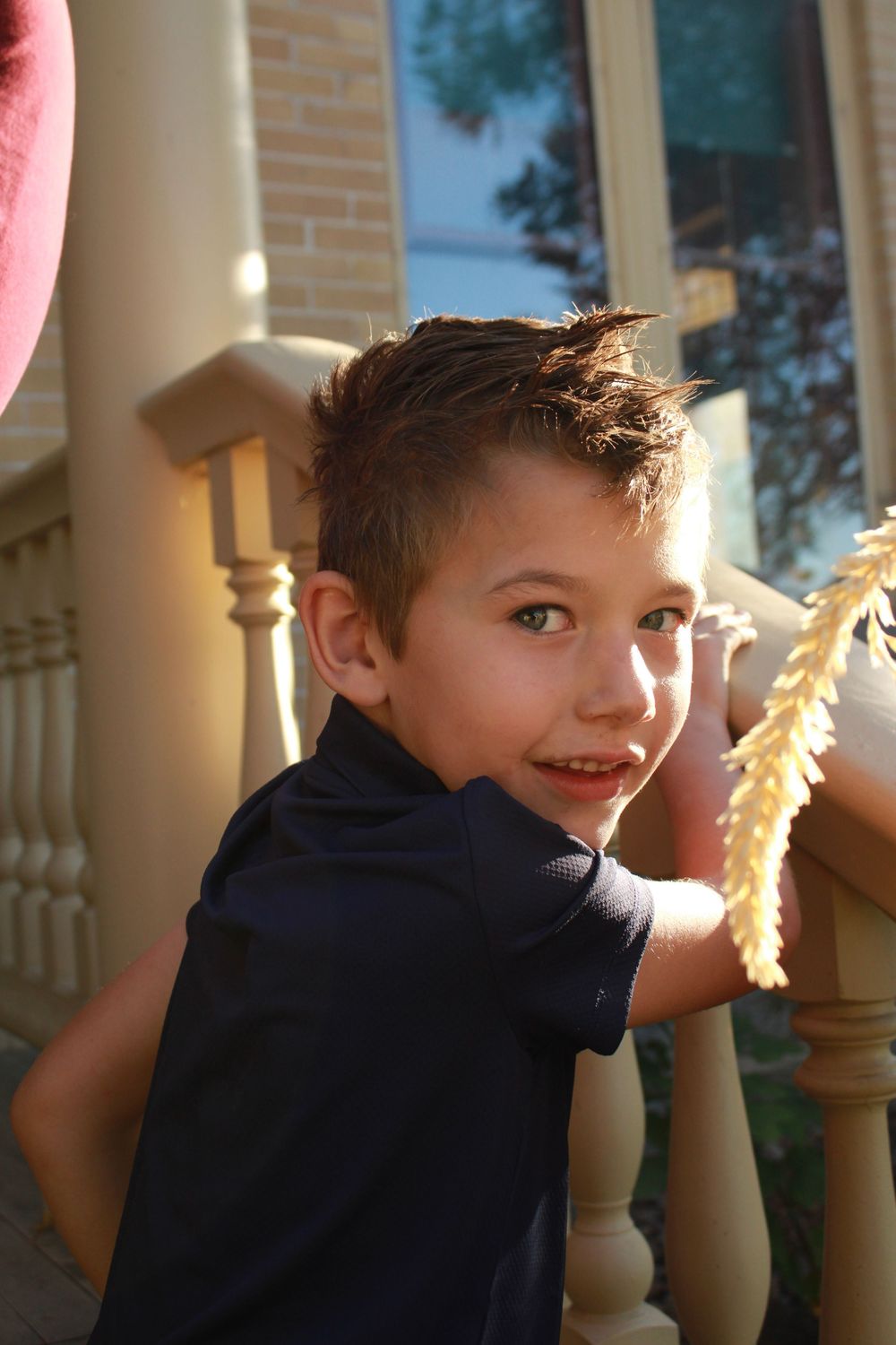 A young child in a navy blue shirt plays with sparklers at dusk near white porch columns.