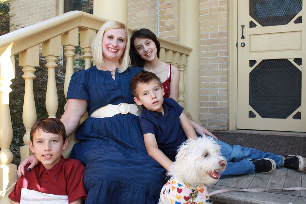 A family sits together on outdoor steps with their small white dog during a portrait session.