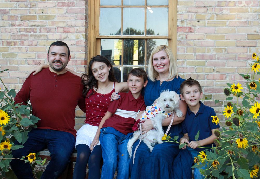 A group sits together on outdoor steps surrounded by blooming sunflowers against a brick wall backdrop.