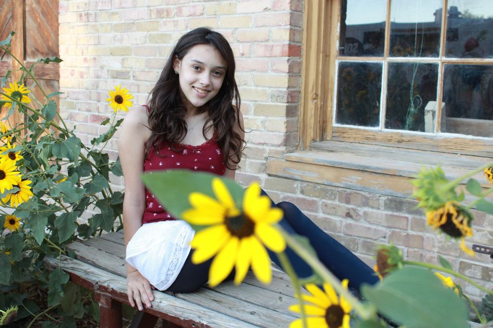 Person in a red dress poses with bright yellow sunflowers against a brick wall backdrop.