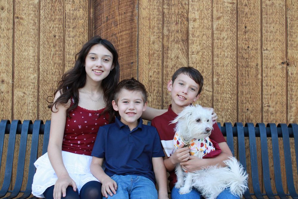 Family and white fluffy dog pose together on wooden deck for casual outdoor portrait.