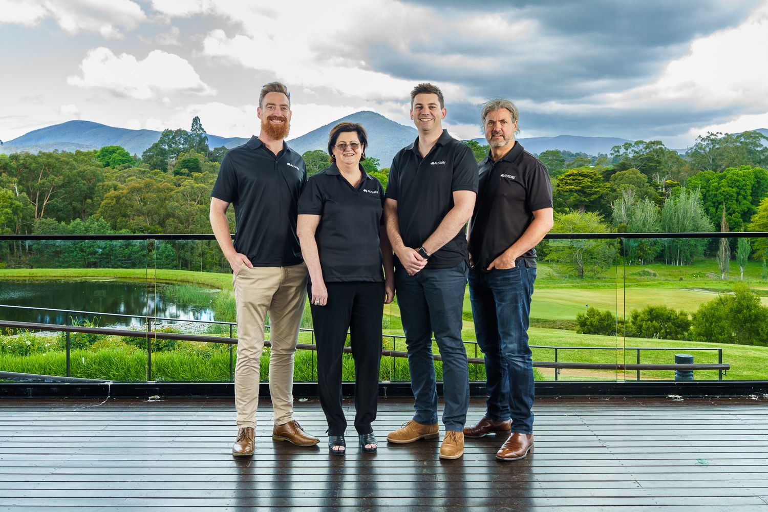 Four colleagues in branded black polos pose outdoors with scenic mountain and golf course backdrop.