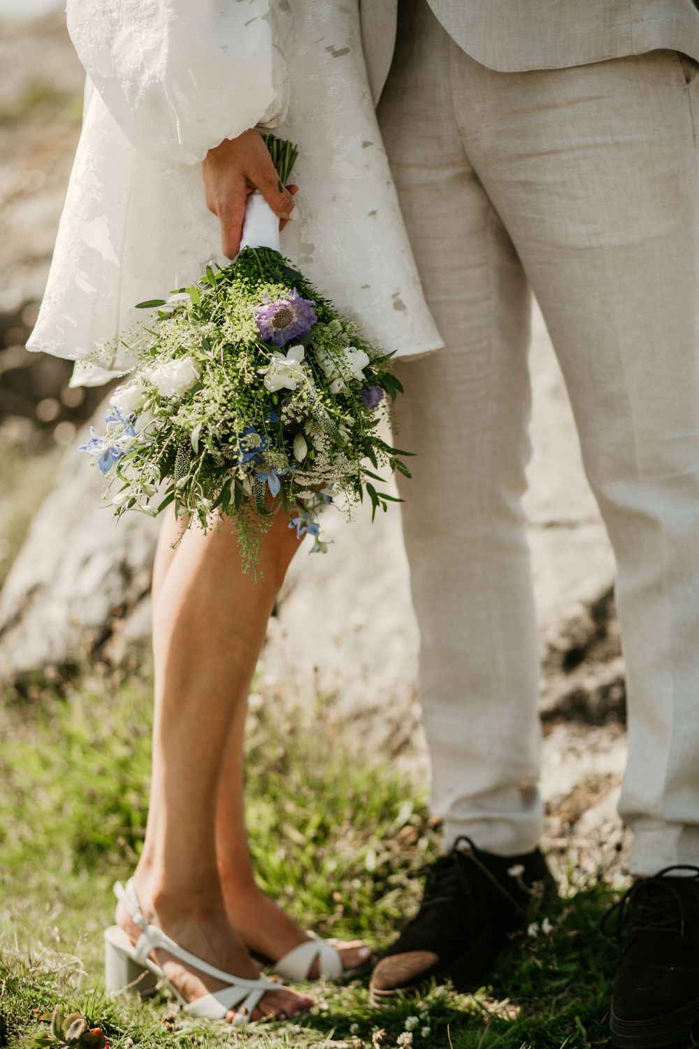 Close-up details of wedding attire showing white dress and bouquet with delicate wildflowers and greenery.