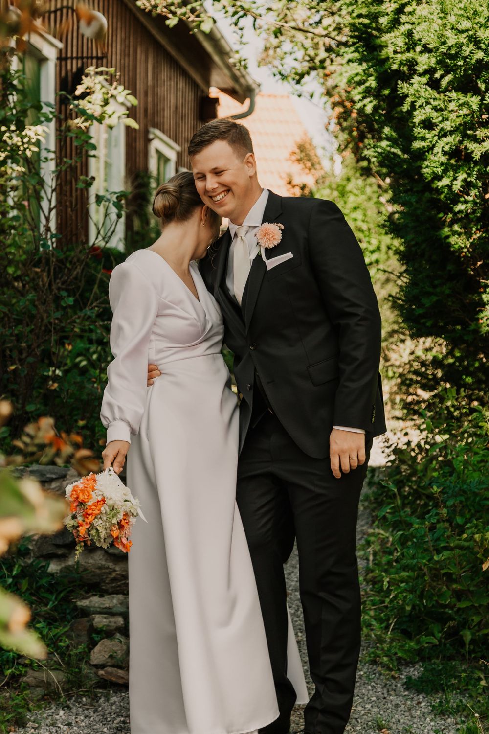 A couple shares a joyful moment together in a garden setting wearing formal black and white attire.