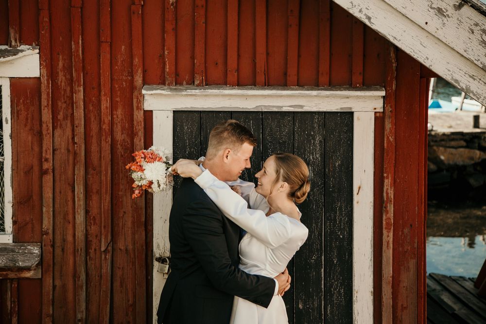 A couple dances together in front of a rustic red barn during a romantic outdoor photoshoot.