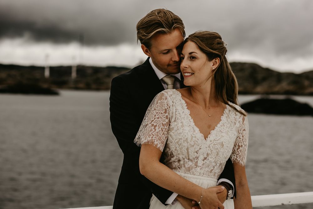 A romantic couple embraces near a moody waterfront on their wedding day in black and white photography.