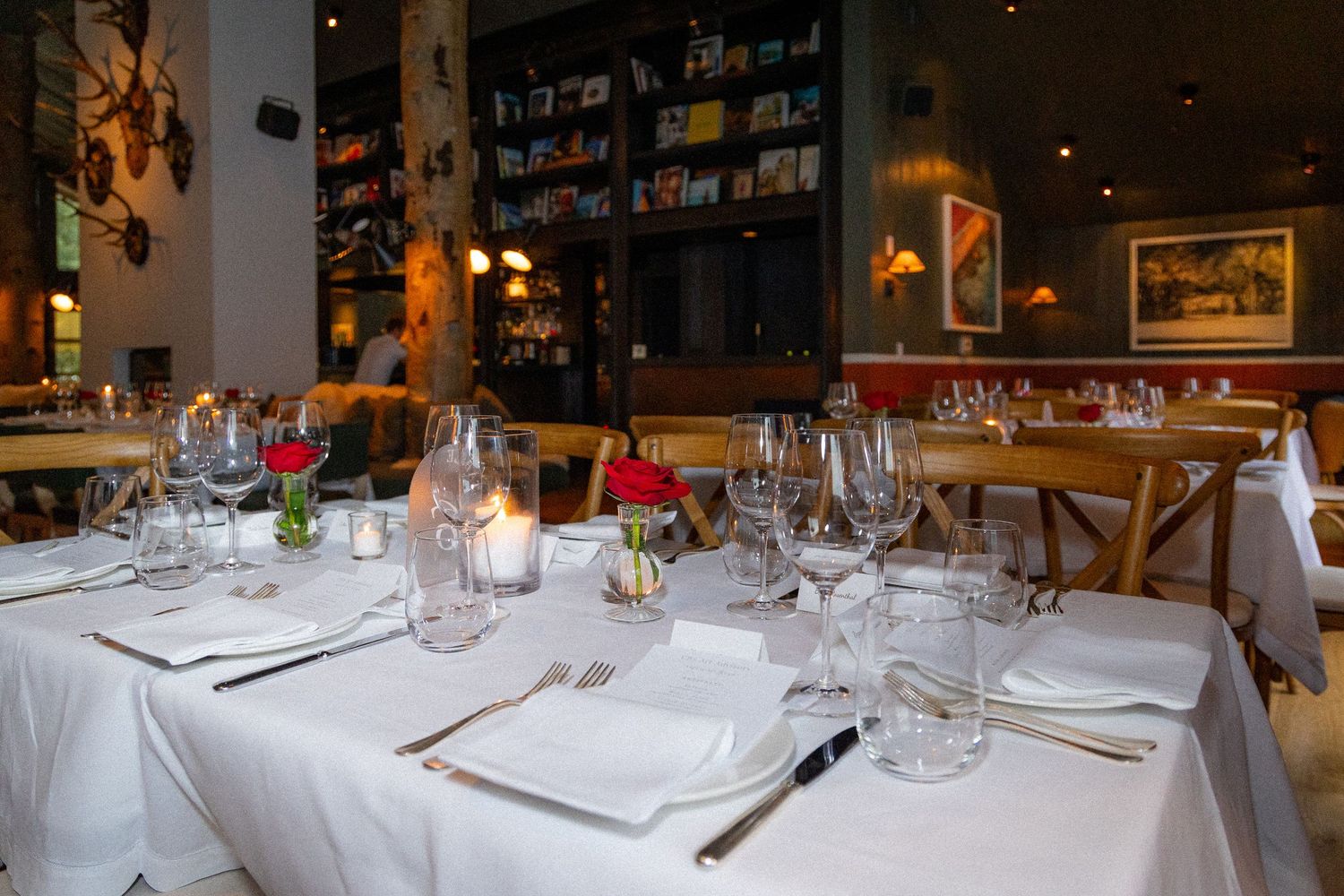 Elegant restaurant interior with multiple round dining tables set with white linens and wine glasses for formal dining.