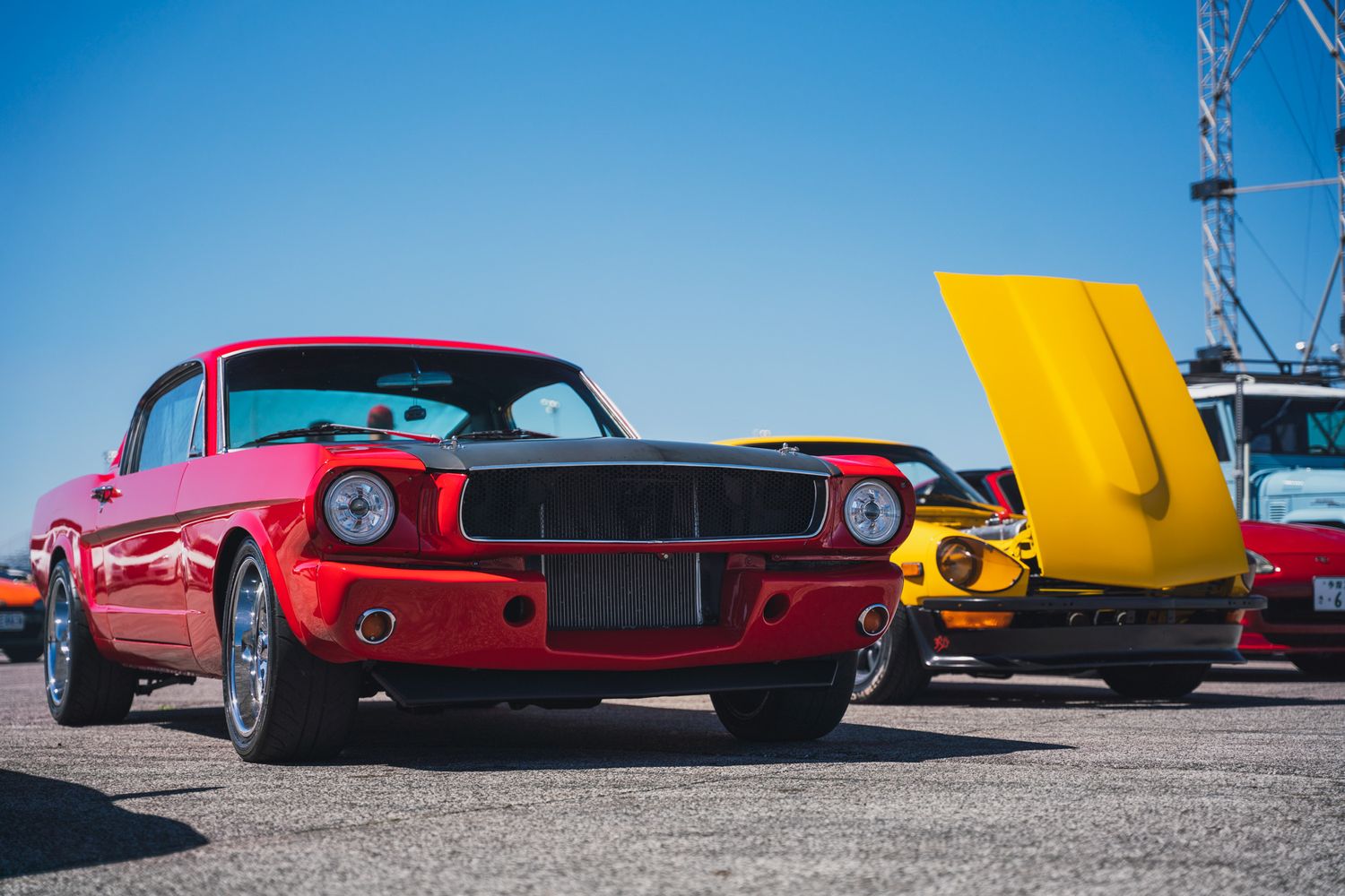 Classic red Ford Mustang displayed at car show next to yellow vehicle.