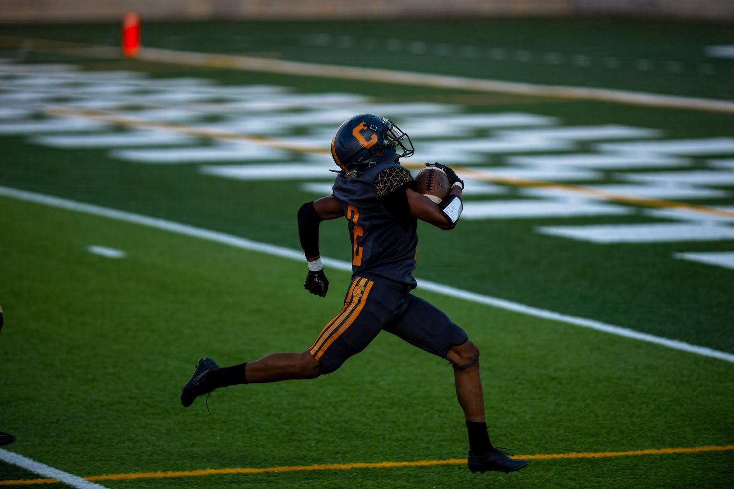 Football player in dark uniform practices kicking technique on field during practice session.