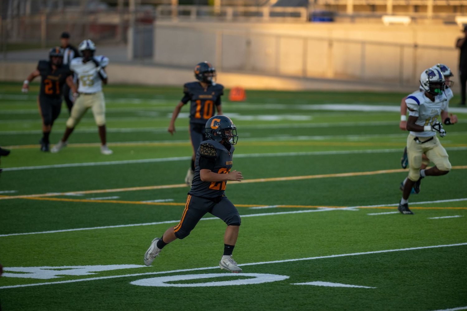 Football players compete on an artificial turf field with bright stadium lights illuminating the evening game action.