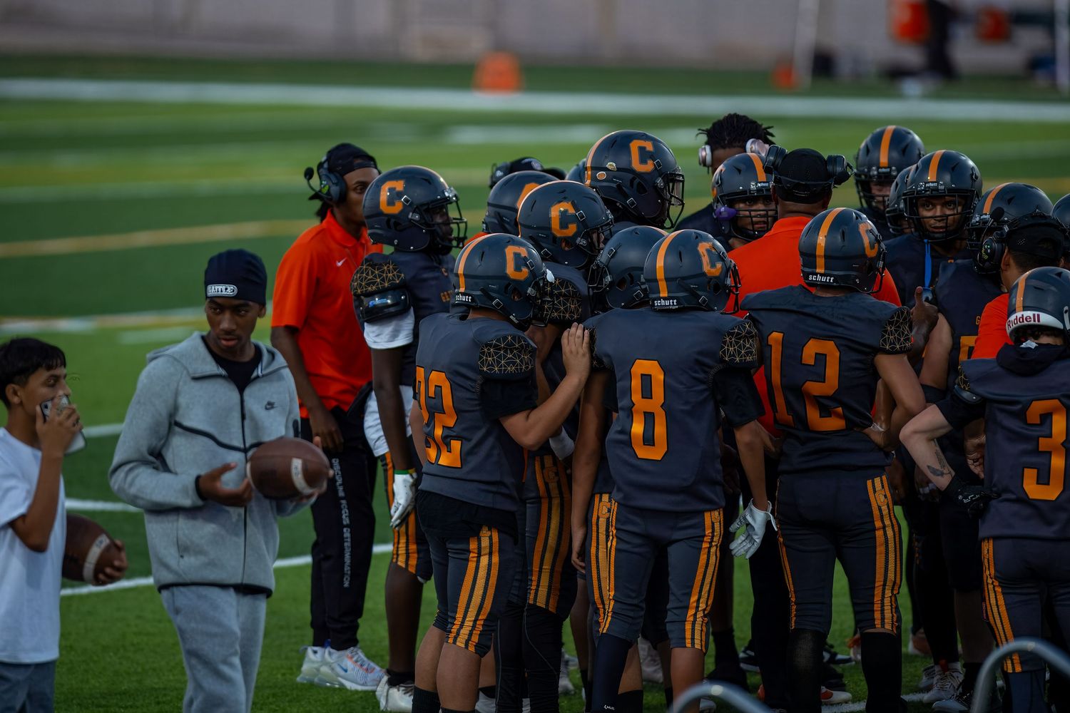 Football players huddle together on the field during a game wearing navy and orange uniforms.