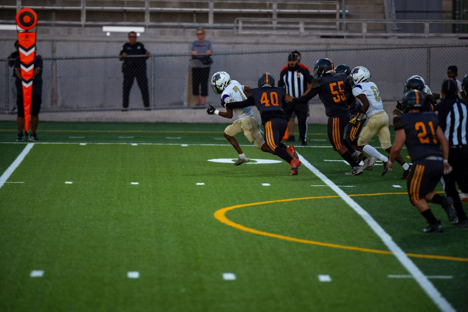 Football players in orange and white uniforms compete during a game on an artificial turf field.