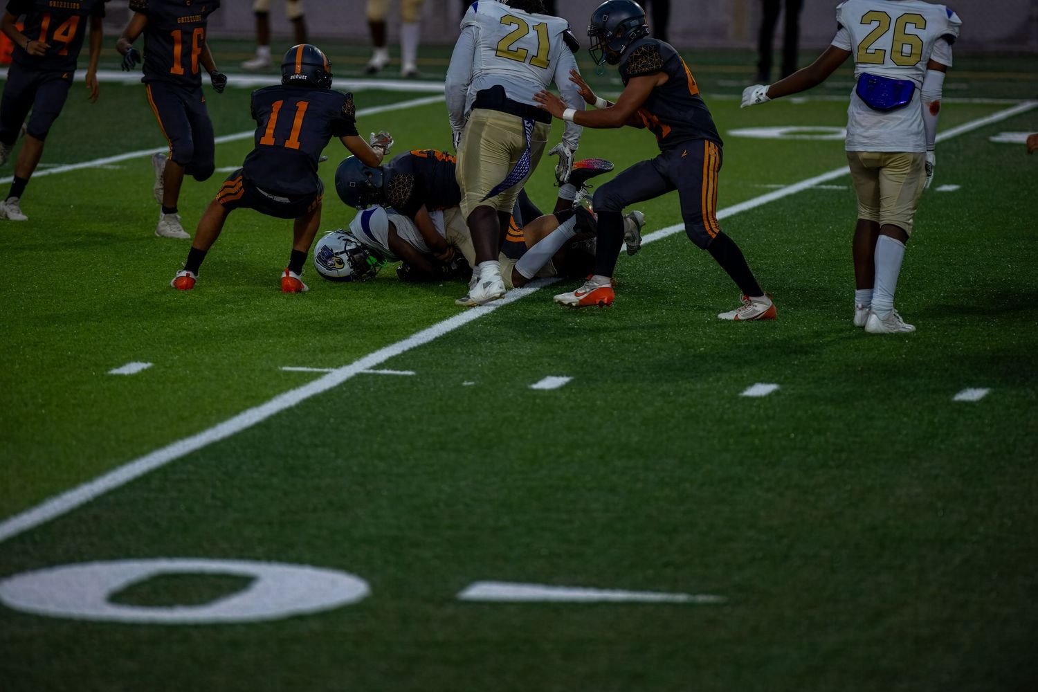 Close-up action shot of football players' legs on a green turf field during a game.
