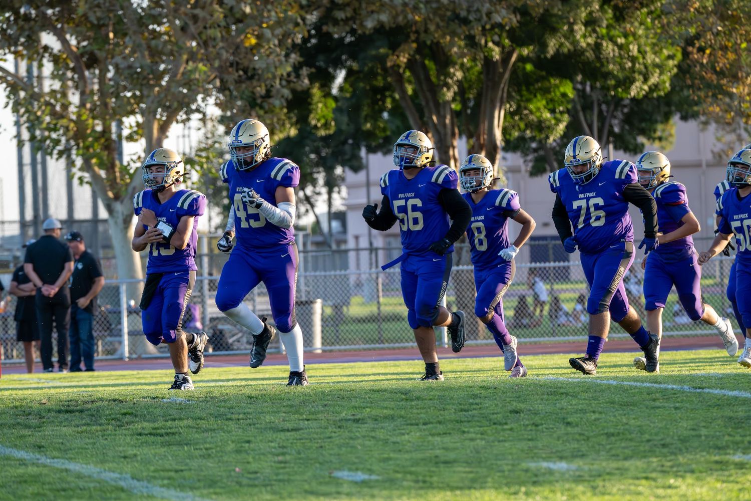 Football players in blue uniforms running drills during practice on a grass field.