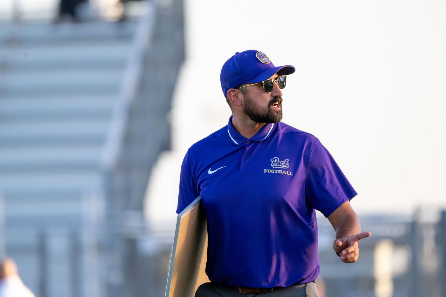 Football coaches in blue team apparel directing players during practice session.