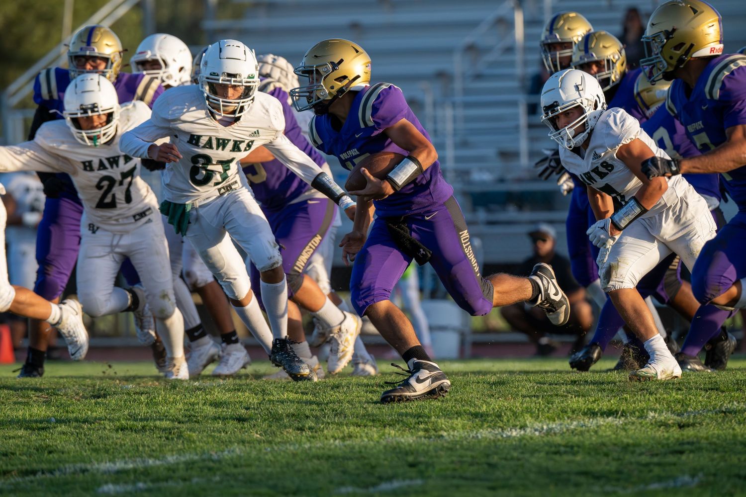 High school football players in purple and white uniforms compete during an intense game on a grass field.