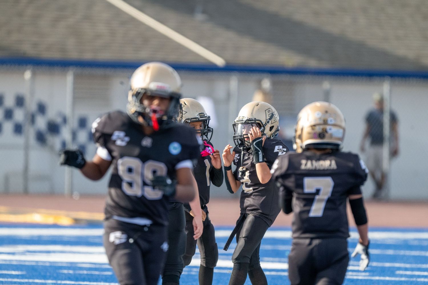 Football players in black uniforms line up in defensive formation on blue artificial turf.