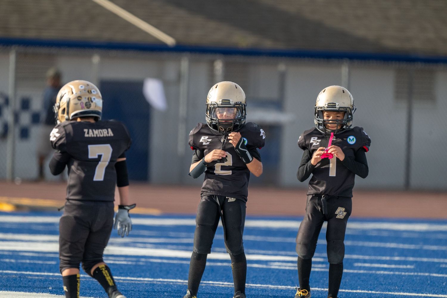 Football team in black and gold uniforms prepares for defensive play on blue field.