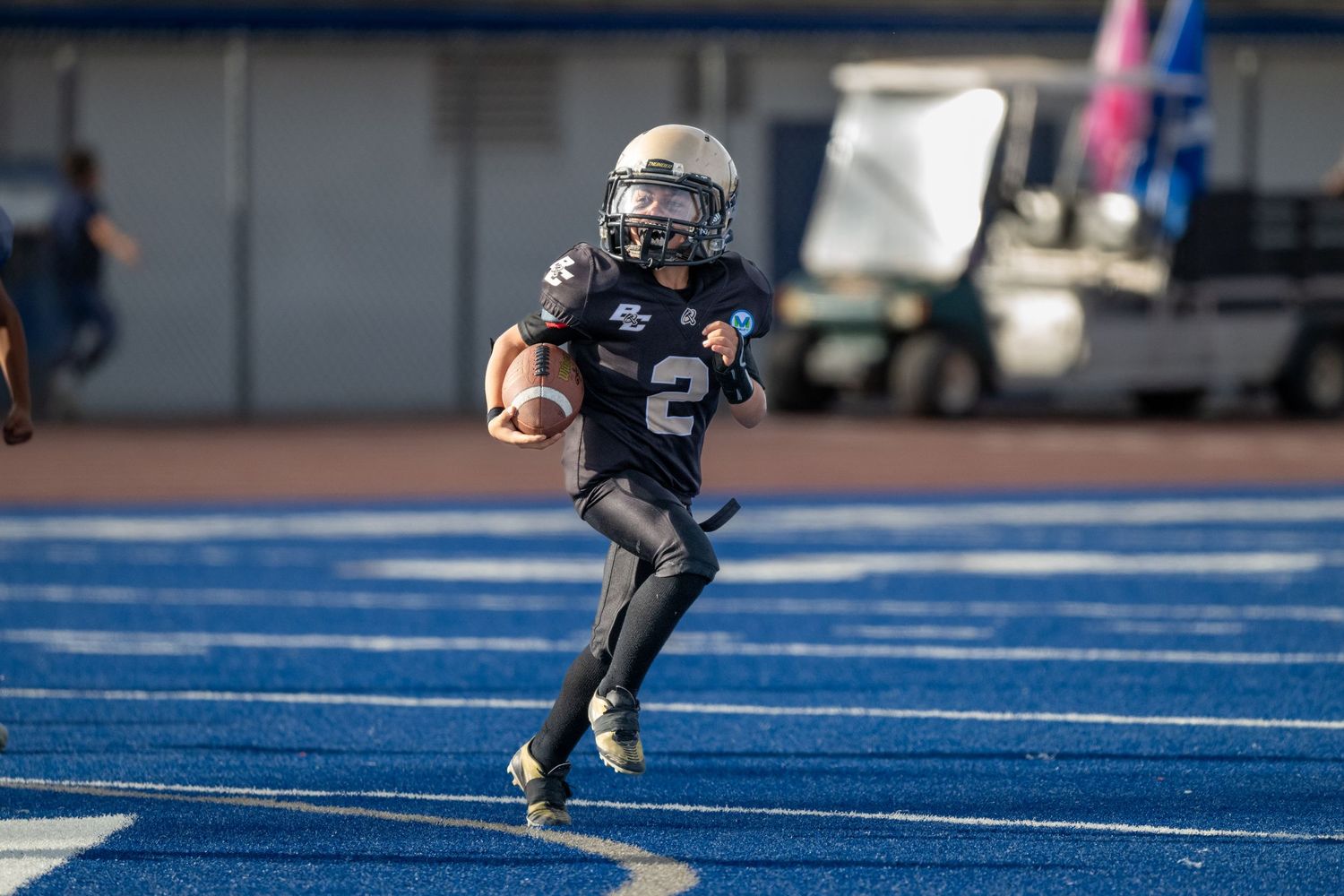 Football players execute defensive plays on vibrant blue artificial turf.