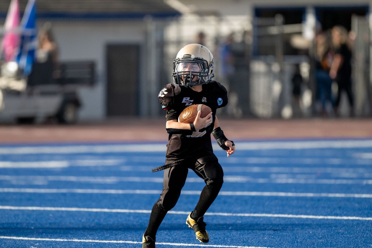 Football players in dark uniforms spread across blue turf field during gameplay.