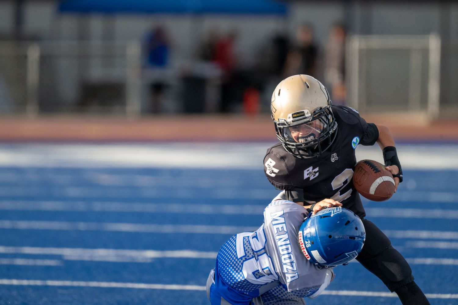 Players compete in a football game on distinctive bright blue turf field.