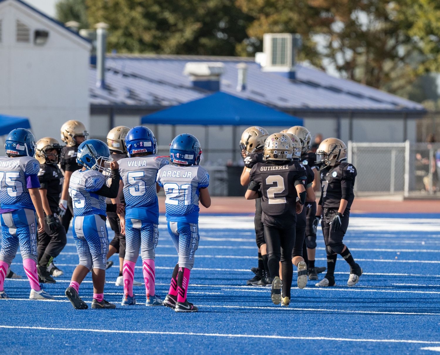 Youth football teams in black and blue uniforms lined up on blue turf field.