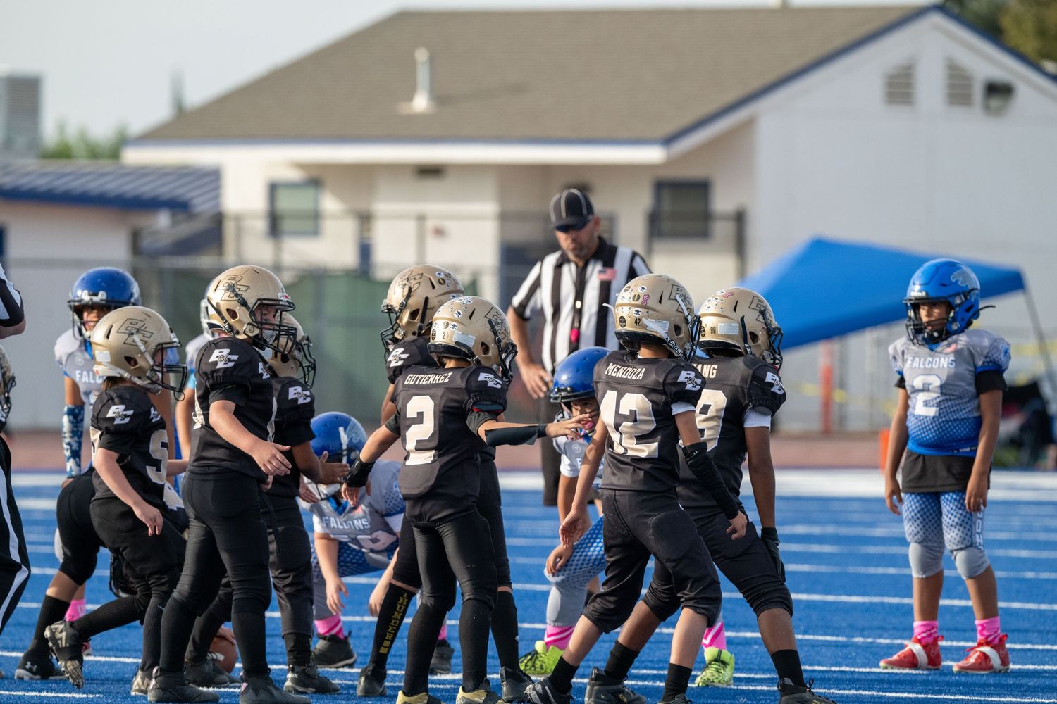 Youth football teams gathered on field with referee during game.