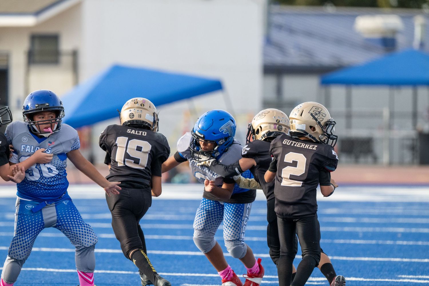 Youth football players in blue and black uniforms facing off on a blue field.