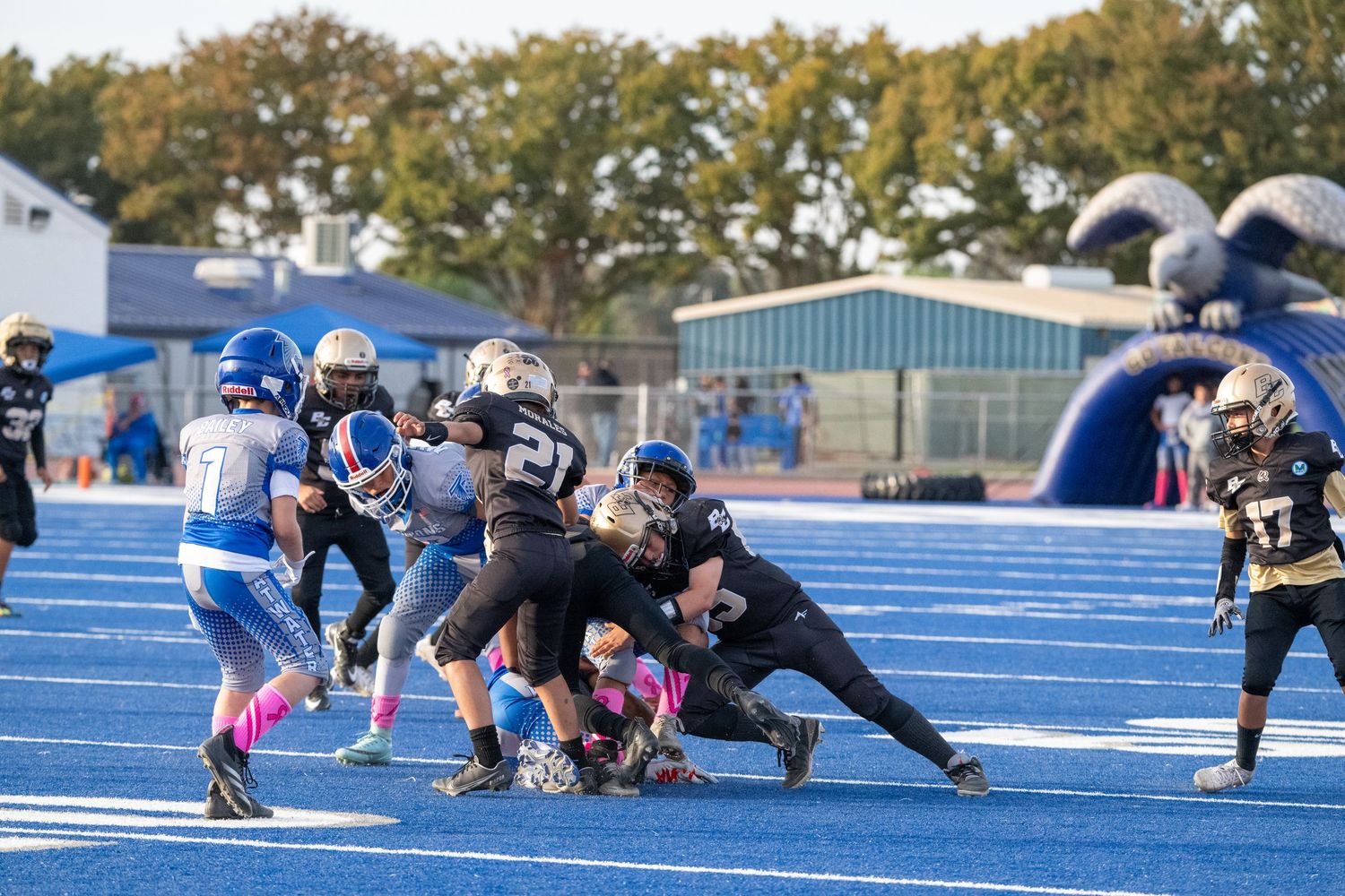 Youth football players tackling during game action on bright blue turf field.