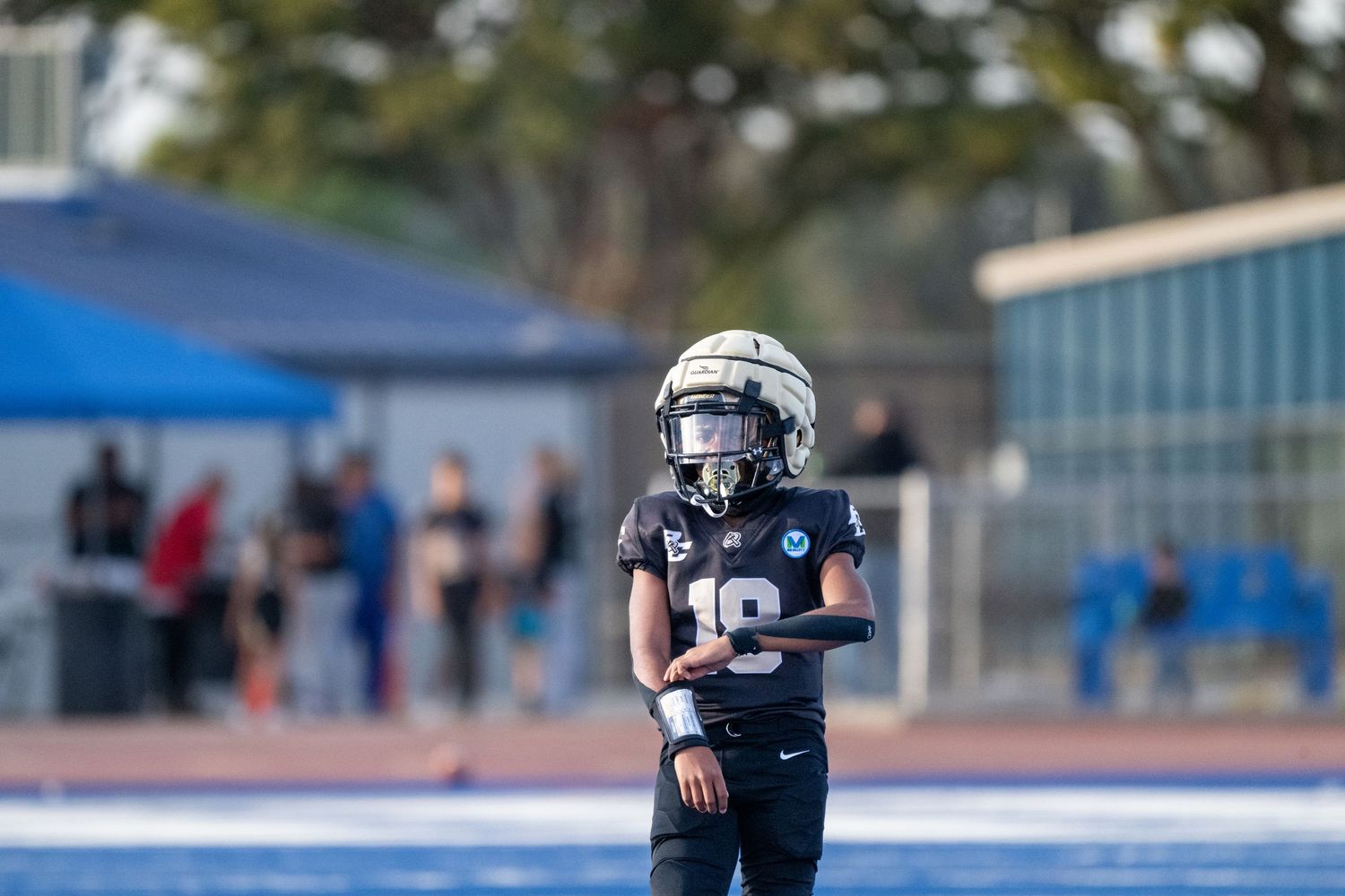 Football team members in black uniforms lined up during practice on blue turf.