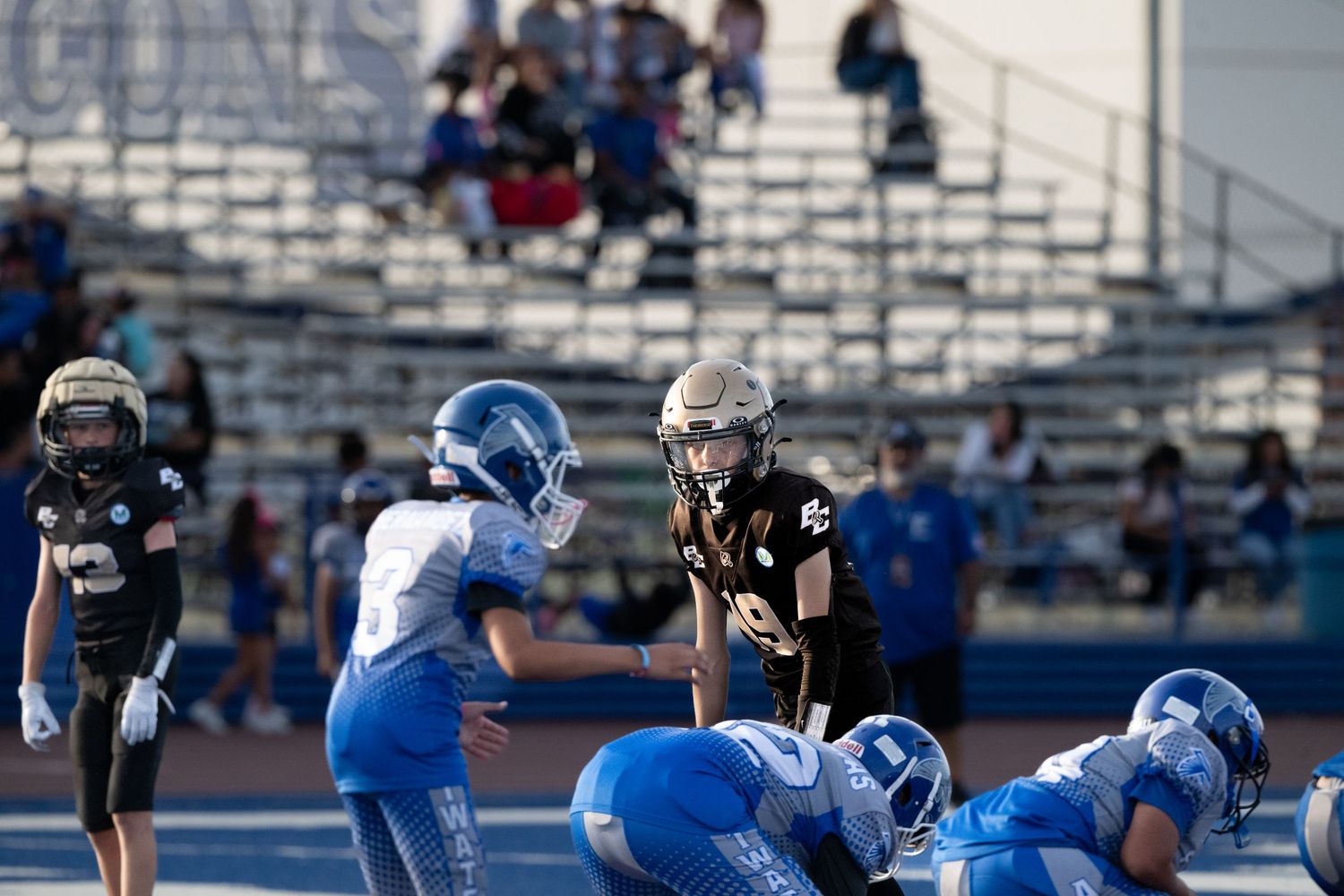 Youth football teams competing in a tackle play on blue turf field.