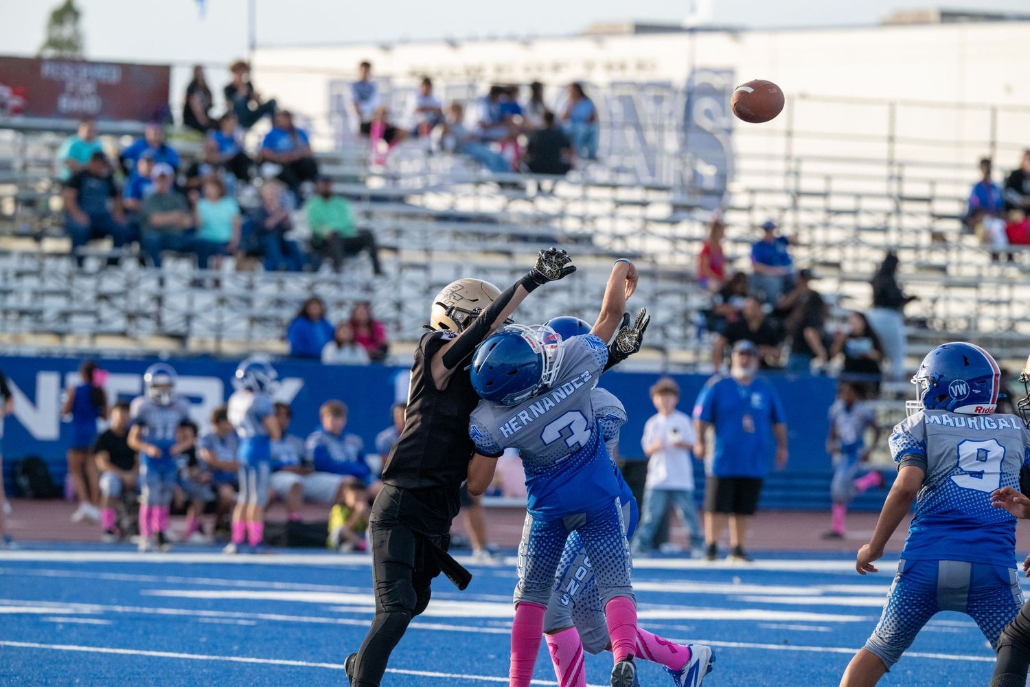 Football player jumping to catch a pass during youth game on blue field.
