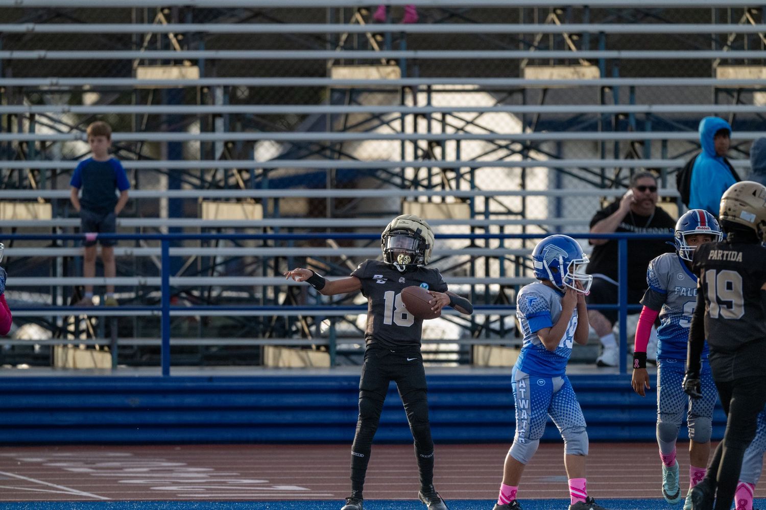 Football teams facing off during game play on bright blue artificial turf field.
