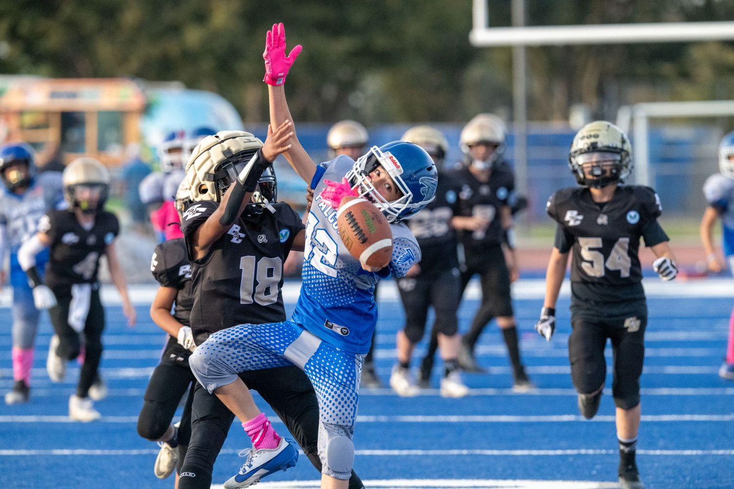 Football players in black and blue uniforms compete on a bright blue turf field during a game.