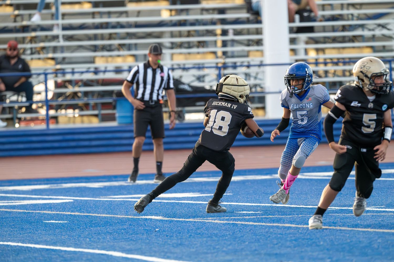 Football players and referee in action on distinctive blue playing field during competitive game.