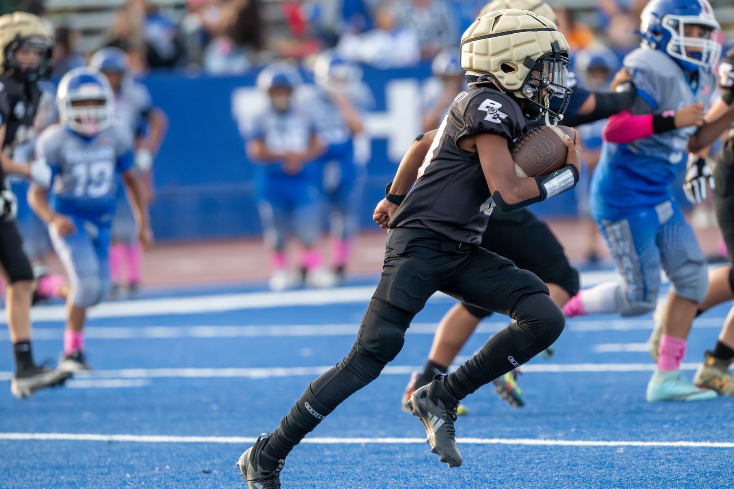 Players from opposing teams face off at the line of scrimmage on a blue football field.