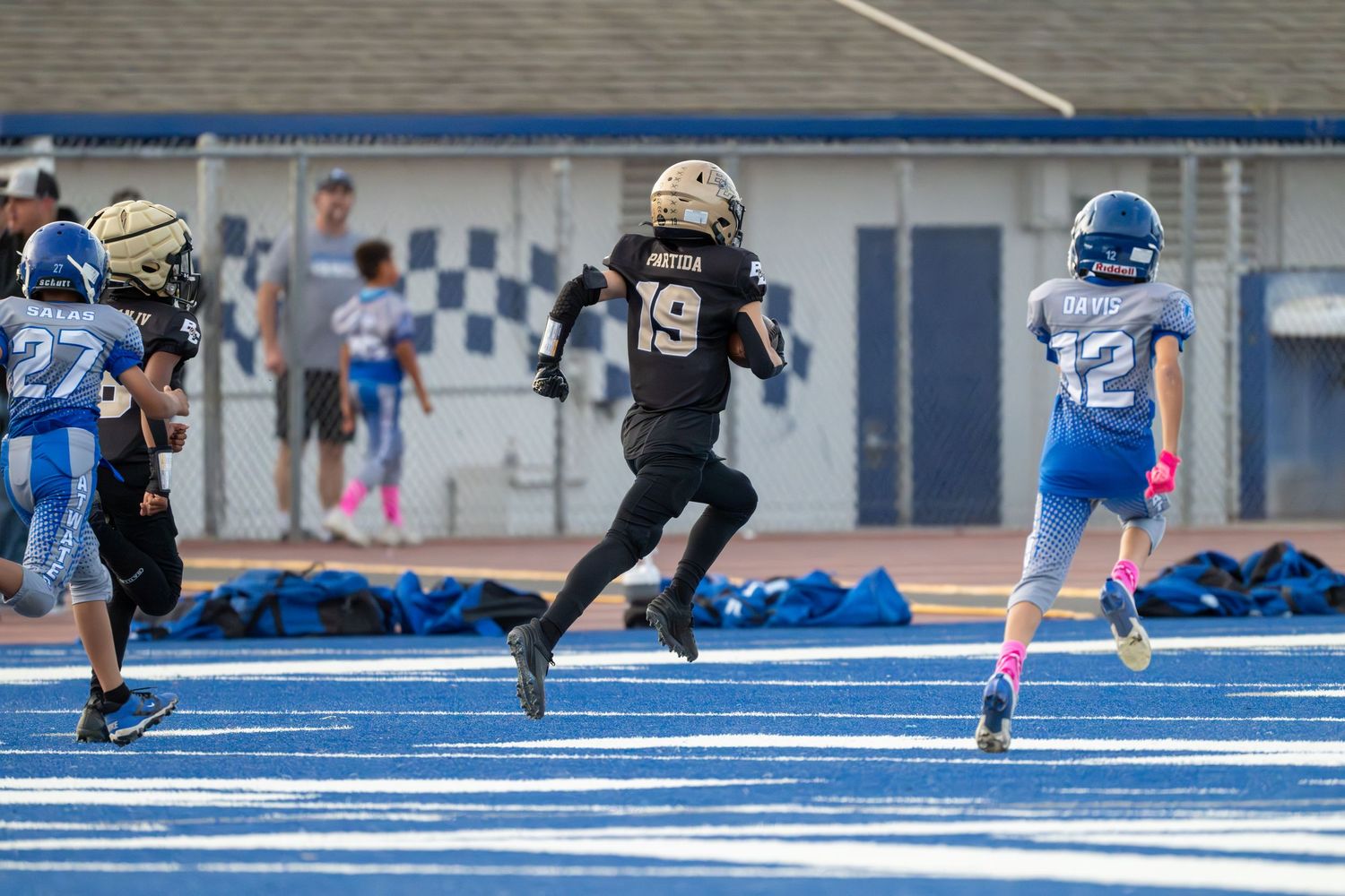 Players in black and gold jerseys face off against opponents on bright blue turf.