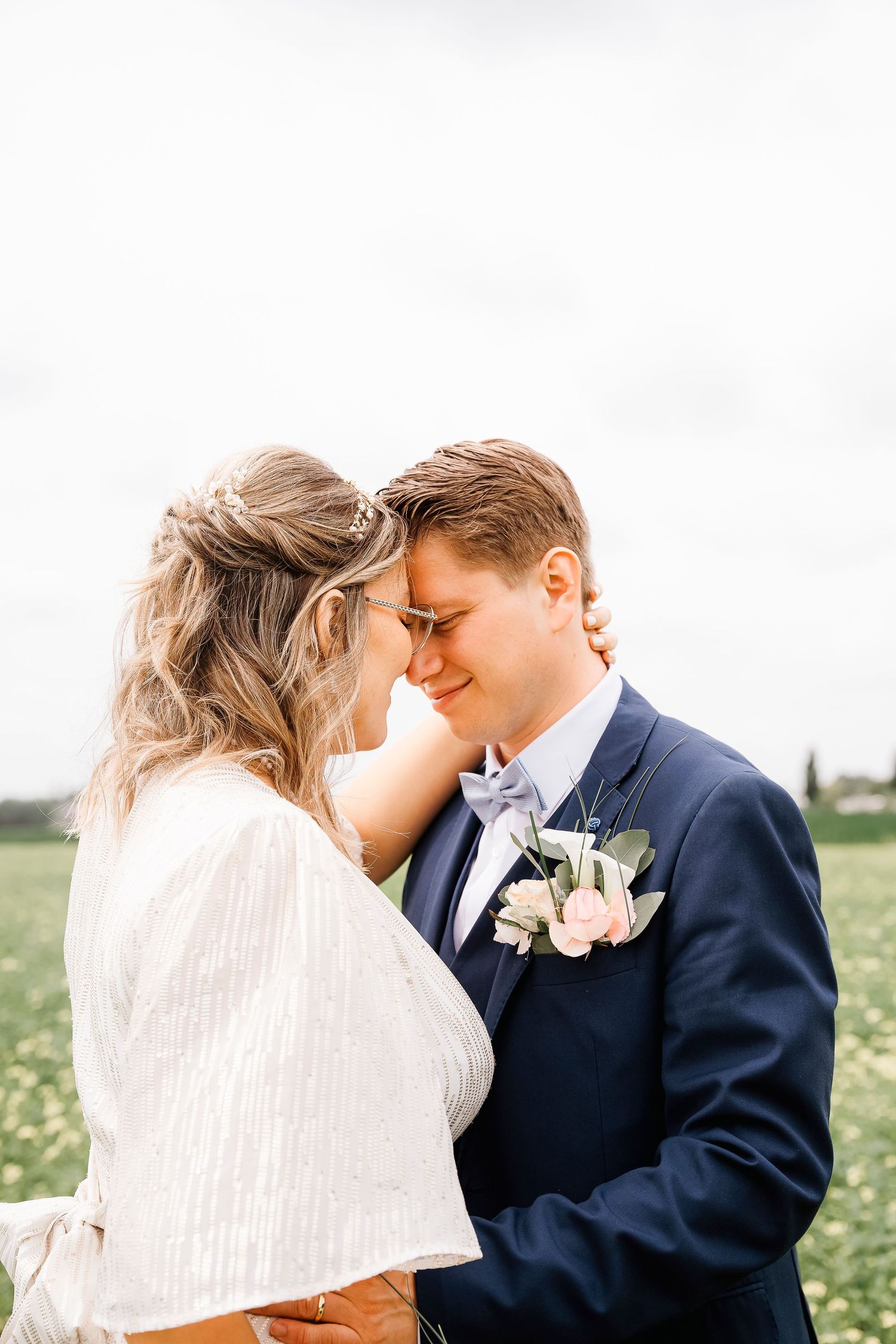 Tender moment between couple in formal attire with white floral boutonniere in field.