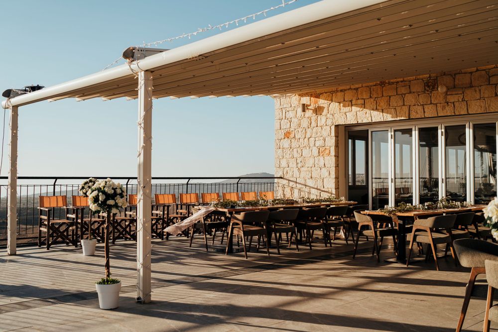 Sunlit terrace wedding venue with wooden chairs and stone walls overlooking a scenic view.