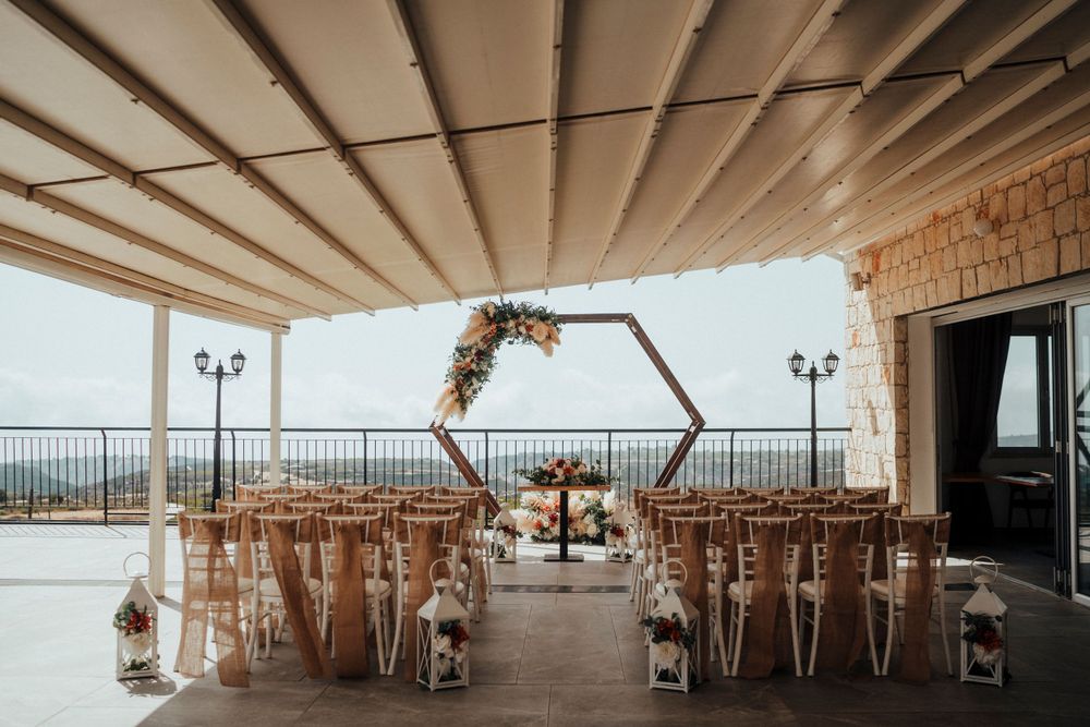 Empty wedding ceremony setup with hexagonal arch and lantern-lined aisle on a covered terrace.