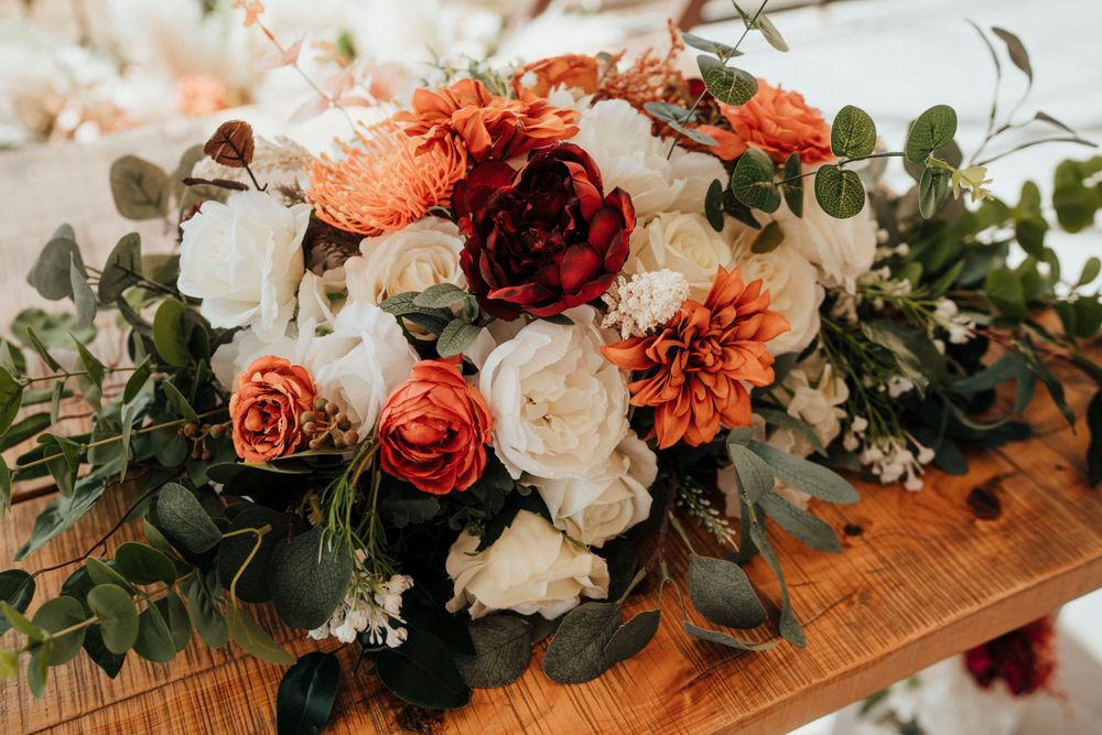 A stunning floral arrangement with coral dahlias, roses, and white flowers on a wooden surface.
