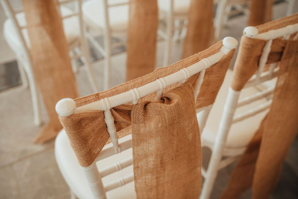 White wooden chairs with burlap sashes lined up for a wedding ceremony.